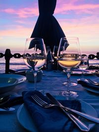 Close-up of wineglasses on restaurant table at beach against sky during sunset