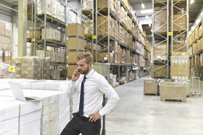 Businessman with laptop and cell phone in warehouse