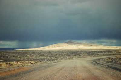 Road passing through land against cloudy sky