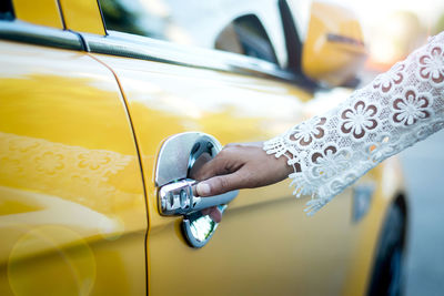 Cropped hand of woman opening yellow car door