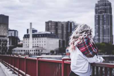 Rear view of woman standing by railing against buildings in city