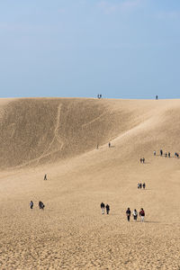 People on sand dune against clear sky