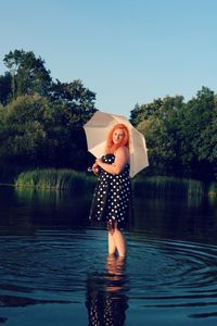 Redhead woman holding umbrella in lake against sky
