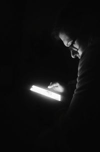 Low section of man holding illuminated light in darkroom