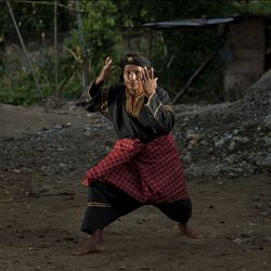 Mature man wearing traditional clothing while performing dance on dirt road