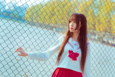 Young woman standing against chainlink fence