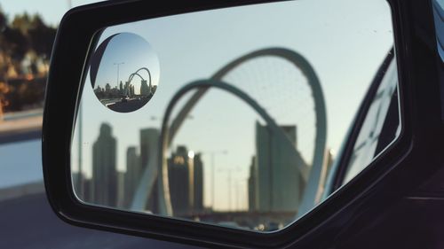 Reflection of al wahda arches and the city of doha skyline in side-view mirror