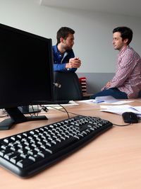 Man with colleague sitting on table at office