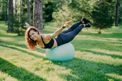 Portrait of woman with arms outstretched exercising on fitness ball in park