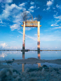 Traditional windmill on wooden post at beach against sky