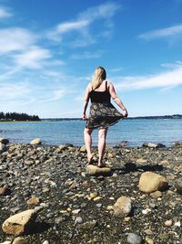 Woman standing on rock by sea against sky