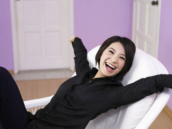 Cheerful woman with arms outstretched sitting on chair at home