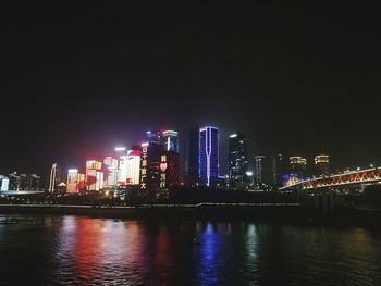 Illuminated buildings by river against sky at night