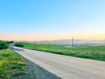 Road amidst field against sky during sunset