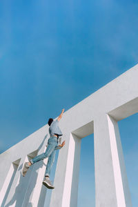 From below of anonymous fearless male hanging on edge of concrete wall and showing risky parkour trick