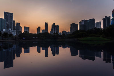 Reflection of buildings in city against sky during sunset