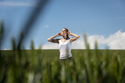 Woman standing in a green field wearing a pair of headphones listening to music.