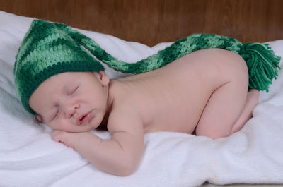 Close-up of naked baby boy wearing knit hat while sleeping on bed