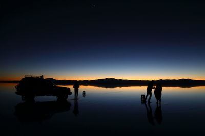 Silhouette people on lake against clear sky during sunset