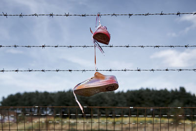 Shoes hanging on barbed wires against sky