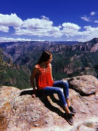 Woman sitting on rock looking at mountains against sky