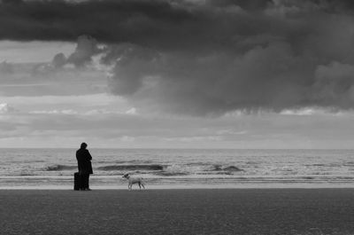 Man with dog walking on beach against sky