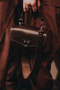 Female hand holding a small leather brown handbag with a strap. brown shades. fancy accessories
