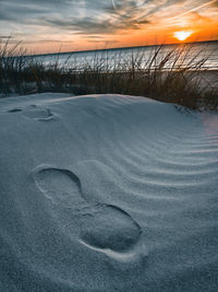 Snow covered land against sky during sunset
