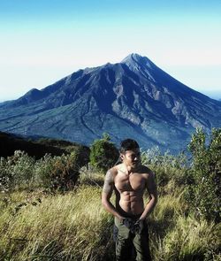 Full length of shirtless man standing on mountain against sky