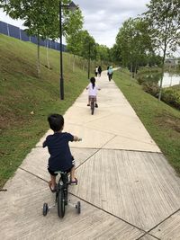 Rear view of kids riding bicycle on footpath