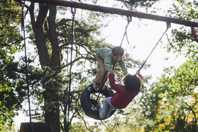 Cheerful boy and girl having fun while swinging at park