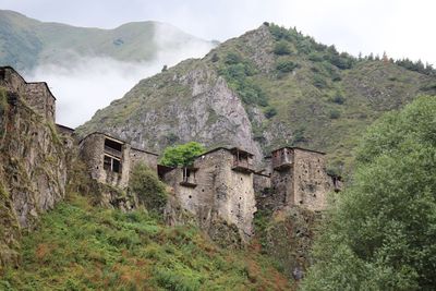 Old house amidst trees and mountains against sky