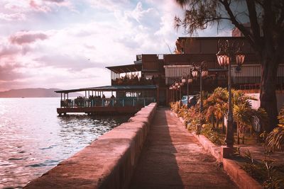 Pier amidst sea and buildings against sky during sunset