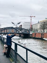 Side view of man feeding seagull standing by canal