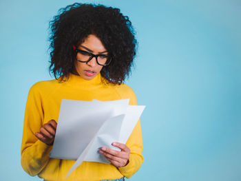 Young woman wearing eyeglasses reading documents against blue background