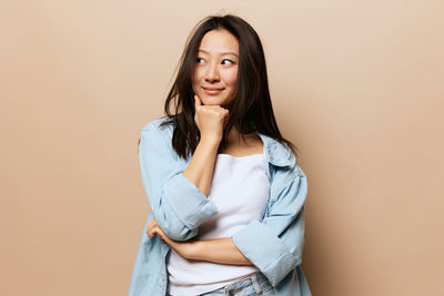 Portrait of young woman standing against yellow background