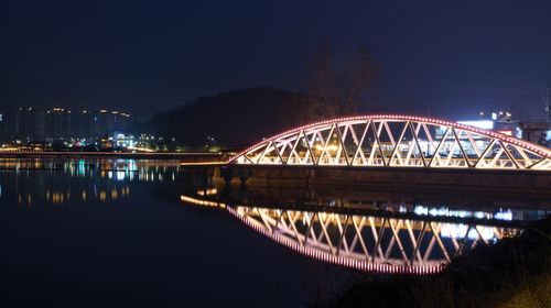 Illuminated bridge over lake against sky at night