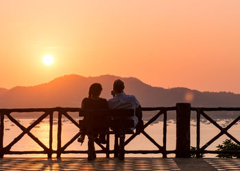 Rear view of silhouette men sitting on mountain against sky during sunset