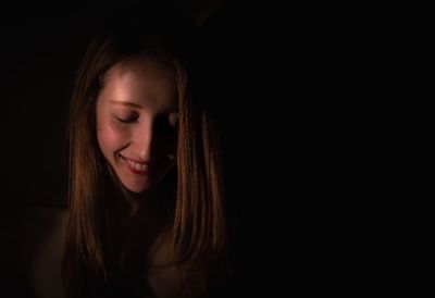 Close-up of smiling young woman against black background