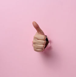 A woman's hand sticks out of the torn hole and shows a gesture okay, thumb up. pink background