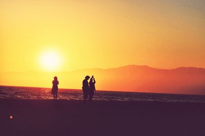 Silhouette men on beach against clear sky during sunset