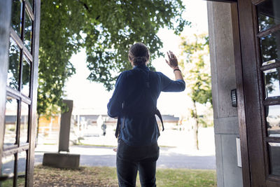 Rear view of mid adult man with baby waving at doorway