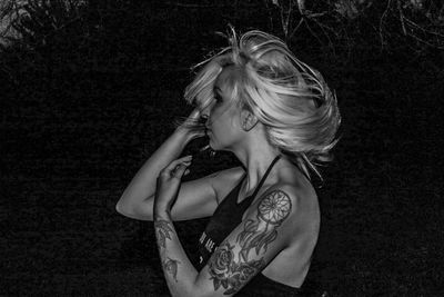 Young woman with tattoos and tousled hair standing against plants