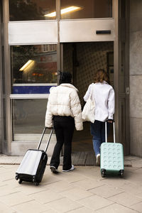 Rear view of young female tourists with wheeled luggage entering in hotel