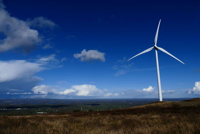 Wind turbine on landscape against blue sky