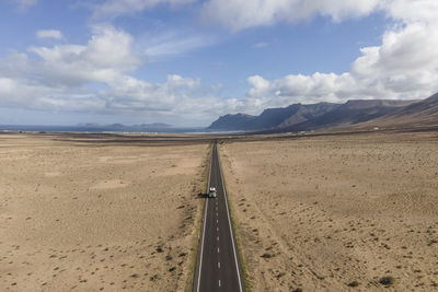 Aerial view of a vehicle driving a straight road crossing the desert valley near teguise, lanzarote