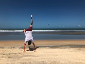 Rear view of man doing handstand at beach against clear sky