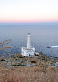 Lighthouse by sea against sky during sunset