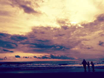 Silhouette people on calm beach at sunset