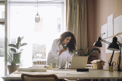 Female architect doing multi-tasking with smart phone and laptop while working at office